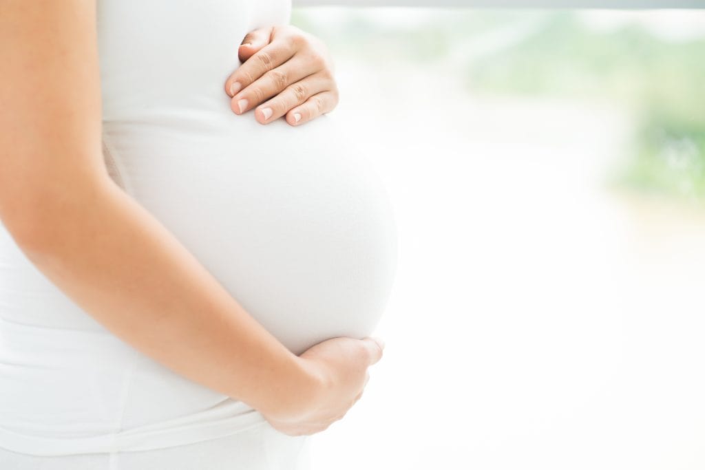 Nahaufnahme einer schwangeren Frau, die ihren Bauch im Vordergrund berührt.
